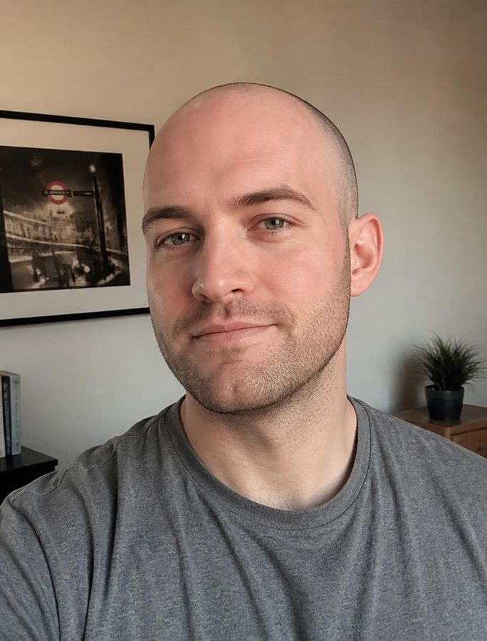 A man in his late twenties with a freshly shaved head and light stubble